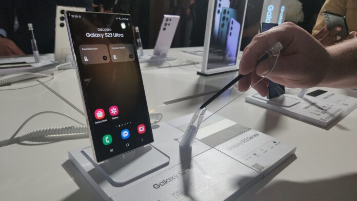 A person holding an S-Pen next to a display of Samsung Galaxy S23 phones.
