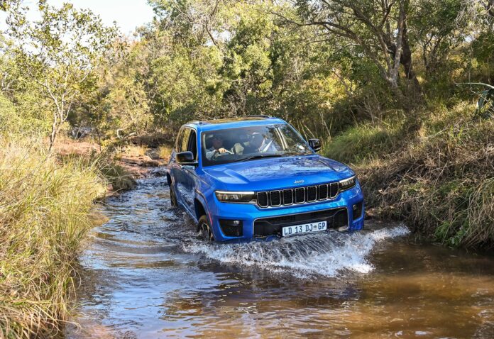 A blue 2023 Jeep Grand Charokee manoeuvring through rough and rugged terrains.