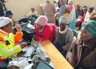 SASSA grant reviews 2026: What pensioners, married beneficiaries and SRD recipients need to know A SASSA official in a yellow and orange vest assists an elderly woman at a laptop during a community outreach in the Eastern Cape, while other seniors listen and interact, highlighting digital training and grant support.