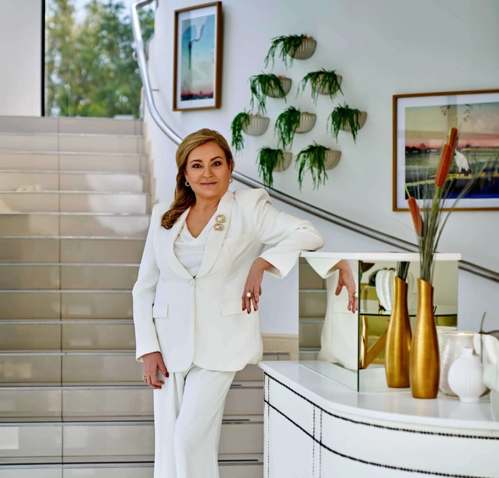 Dr Maureen Allem standing in a white suit at a modern Skin Renewal clinic with gold decor and wall art in the background.