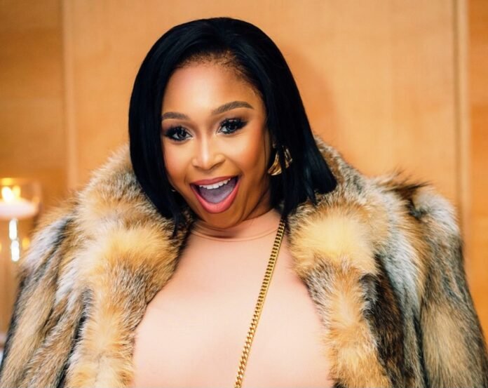 Minnie Dlamini smiling, wearing an elegant fur coat and gold chain.