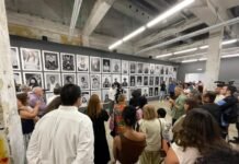 When South African art travels, the world listens — Zanele Muholi in Panama A wide shot of a crowded art gallery with an industrial ceiling, featuring a massive wall of black and white portrait photography.