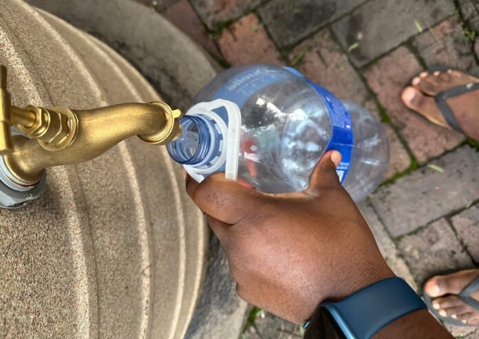 Person filling plastic bottle from outdoor tap during Johannesburg water shortage.