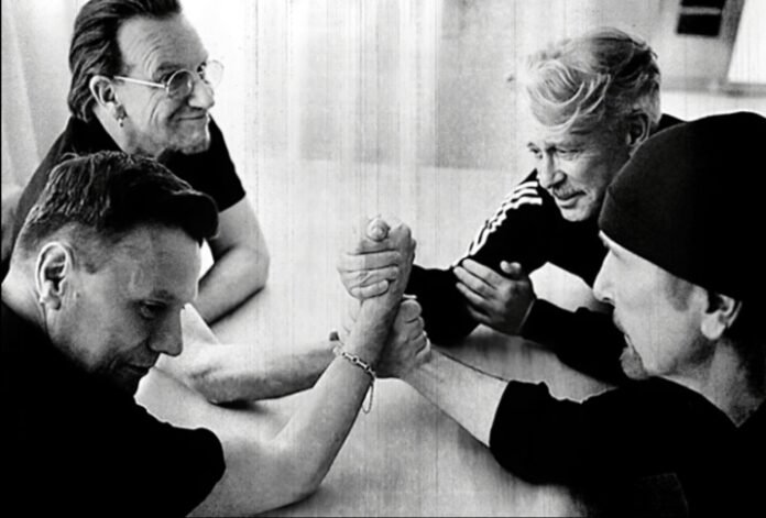 U2 members in a black-and-white arm-wrestling match, capturing a playful moment of camaraderie.