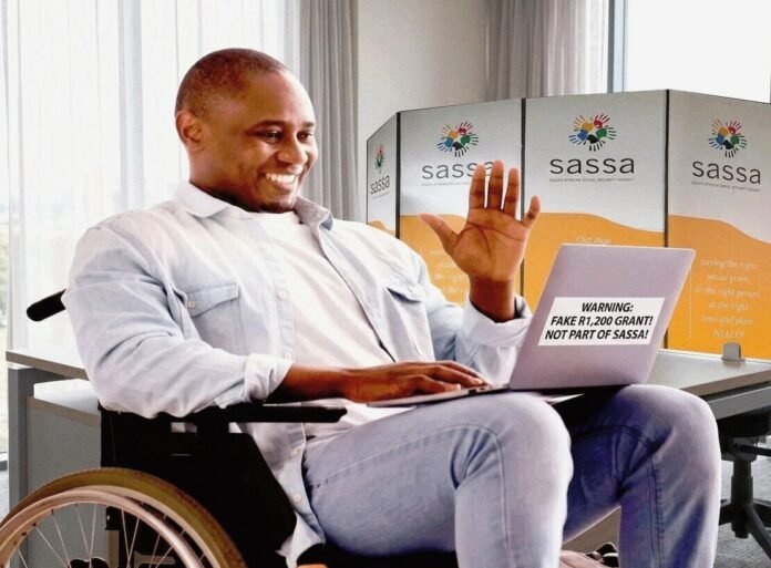 A smiling man in a wheelchair waves at his laptop, which displays a warning sticker reading 