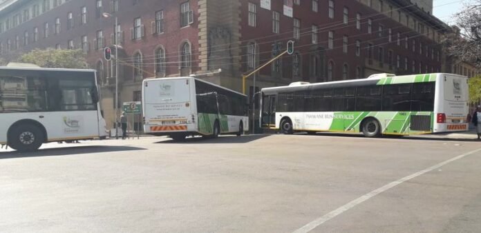Three Tshwane Bus Service buses at a city junction in front of a municipal building, highlighting disruptions from local fuel shortages in South Africa.