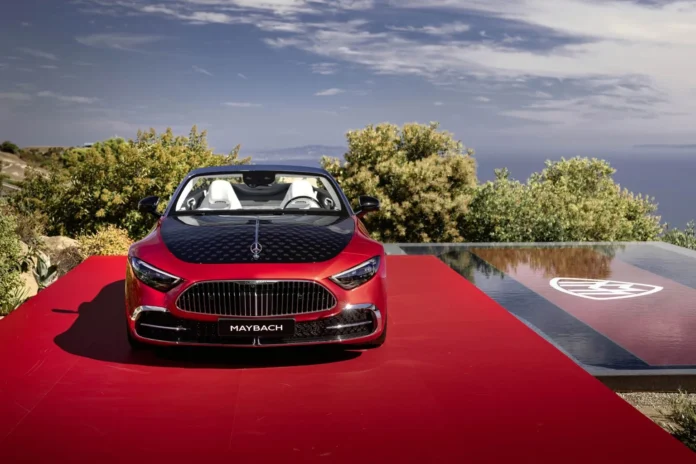 Front view of the red Mercedes-Maybach SL 680 Monogram Series roadster on a red stage overlooking the ocean, displaying the chrome grille and upright bonnet star.