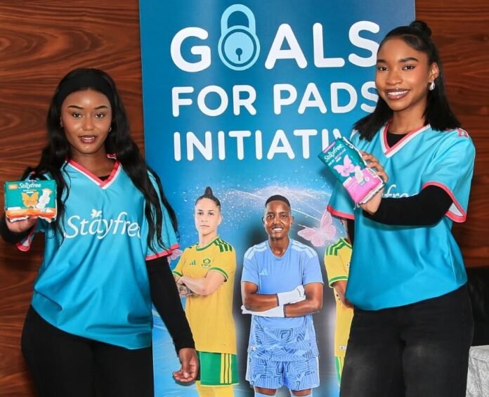 Two Goals 4 Pads female campaign representatives hold Stayfree sanitary pad packs beside a large campaign banner at the launch event in Johannesburg