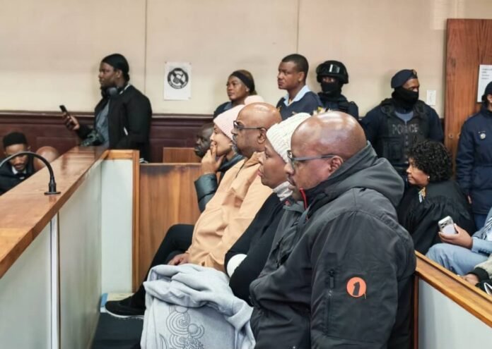 Imogen Mashazi and three co-accused sit in the Germiston Magistrate's Court as SAPS officers stand behind them.