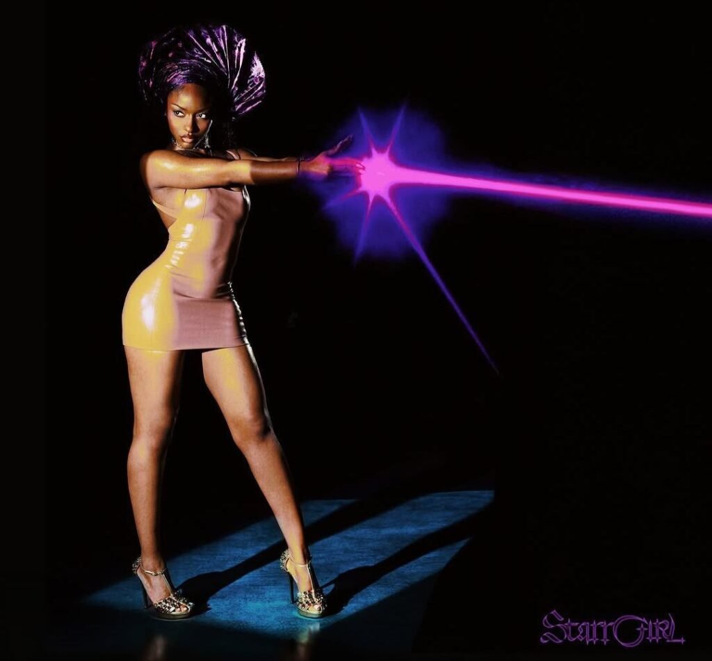 Ayra Starr stands in a yellow dress, projecting a bright purple beam against a black background.