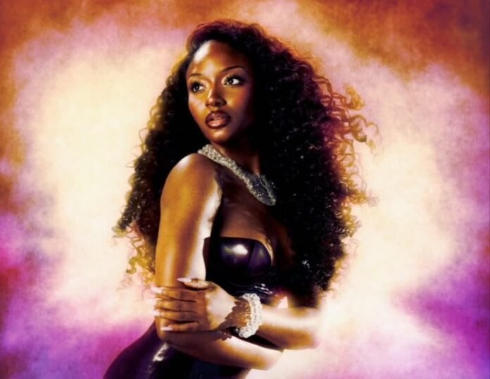 Ayra Starr poses in a black outfit with long curly hair against a glowing purple and pink backdrop.