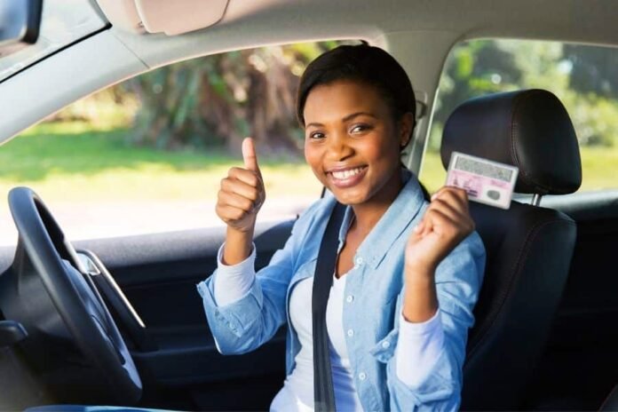 Smiling woman in a car giving a thumbs up while holding her driving licence card.