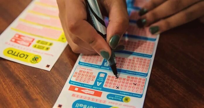 Person marking numbers on a South African National Lottery playslip beside another ticket on a wooden table.