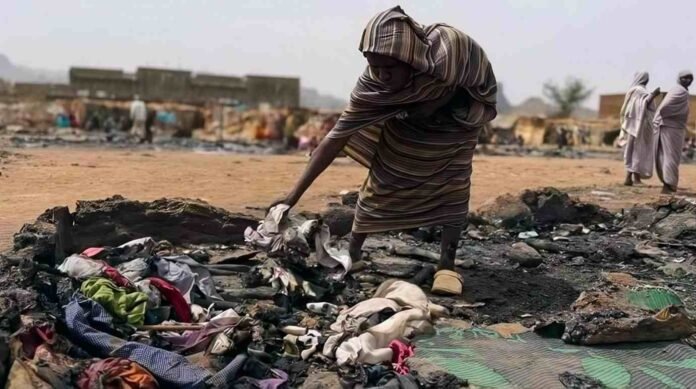 A person stands among charred debris and burned belongings in a devastated area of Sudan’s Darfur region.