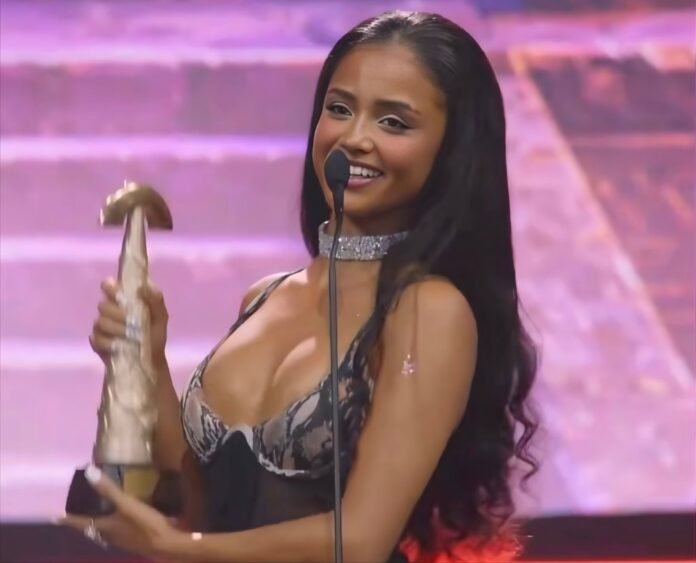 Tyla smiles at a microphone while holding her SAMA32 trophy on stage.