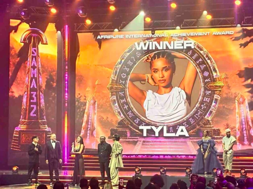 Tyla's portrait fills the SAMA32 stage screen as artists stand beneath it during her award presentation.