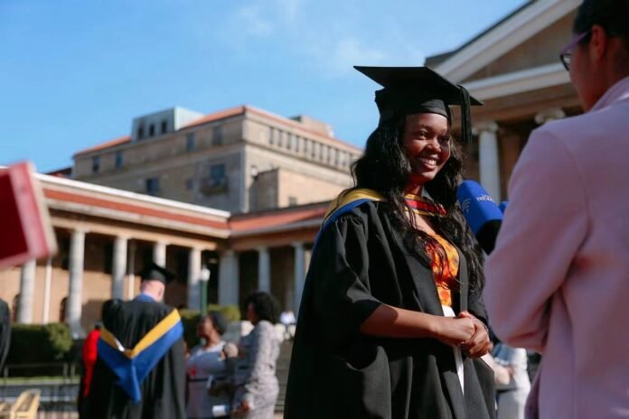 Smiling UCT graduate in cap and gown interviewed during a University of Cape Town graduation ceremony.
