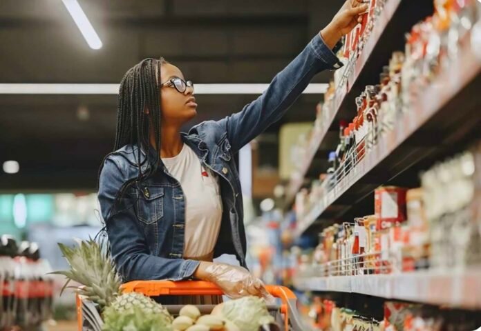 Woman browsing shelves with a trolley of fresh produce in a South African grocery store.