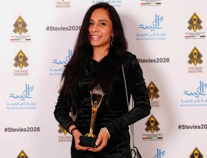 Aeysha Coetzee-Ismail smiling and holding a gold Stevie Awards trophy in front of a #Stevies2026 backdrop