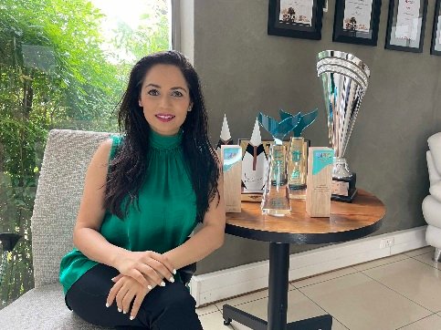 Sarika Modi seated beside a table displaying Triple Eight marketing industry awards