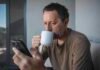 The link between coffee and concentration Man squints at his phone while sipping coffee from a white mug
