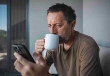 The link between coffee and concentration Man squints at his phone while sipping coffee from a white mug