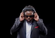 DJ MidTempo: How Tech & Property CEO Theo Mseka Makes Afro House on the Move DJ MidTempo Theo Mseka in a black suit holding headphones for his Cheza Kidogo debut Afro House album.