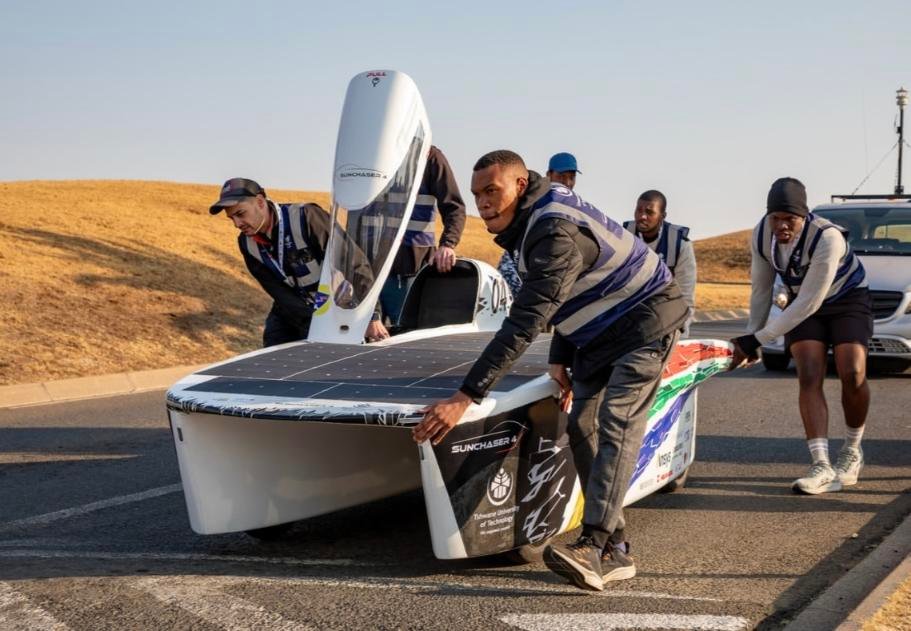 TUT Solar Car team members working on the SunChaser 4 solar-powered vehicle on a road.
