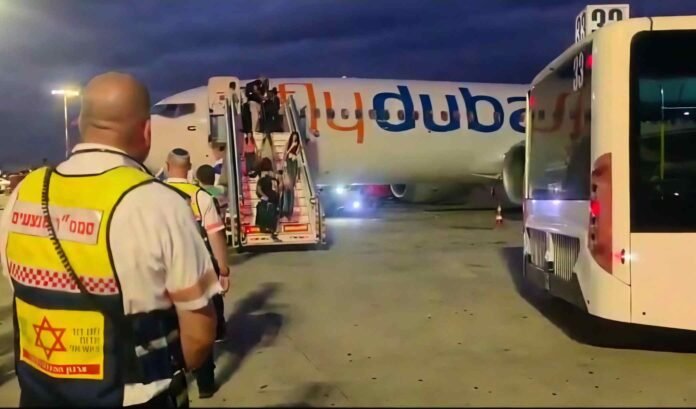 Flydubai passengers walk down aircraft stairs at night as a Magen David Adom paramedic watches beside an airport bus