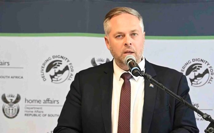 Leon Schreiber speaks into a microphone in front of a Department of Home Affairs banner.